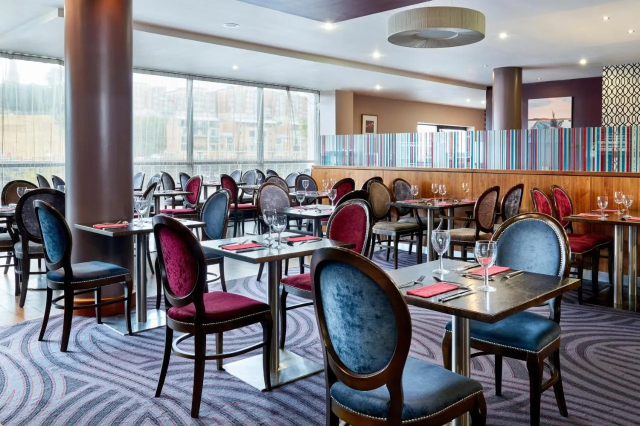 a restaurant with tables and chairs and windows at Leonardo Hotel Newcastle Quayside in Newcastle upon Tyne
