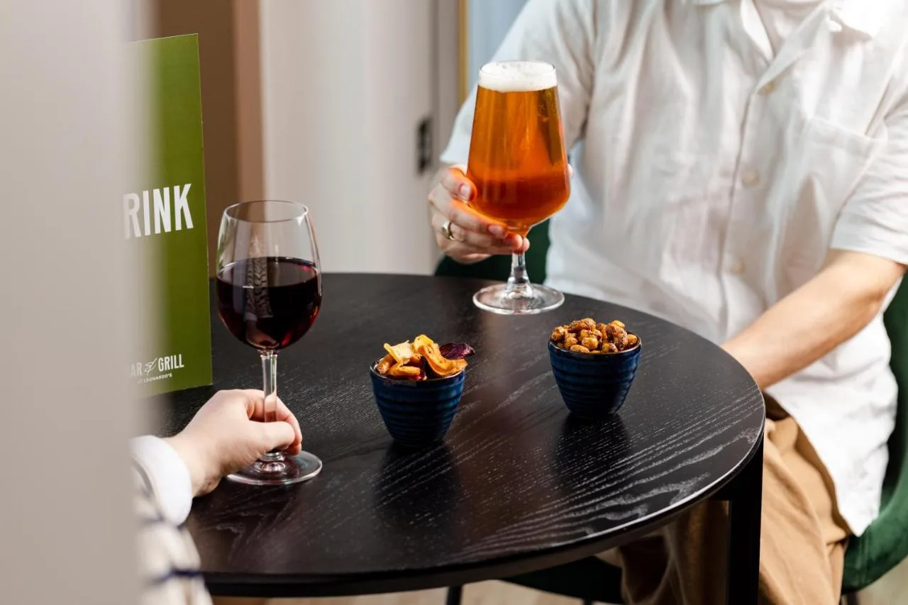 two people sitting at a table with two glasses of wine and snacks at Leonardo Hotel Newcastle Quayside in Newcastle upon Tyne