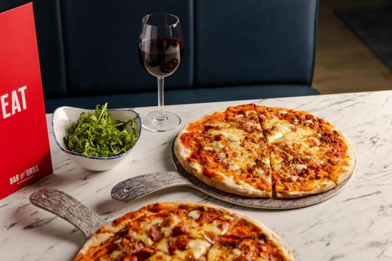two pizzas sitting on a table with a glass of wine at Leonardo Hotel Newcastle Quayside in Newcastle upon Tyne